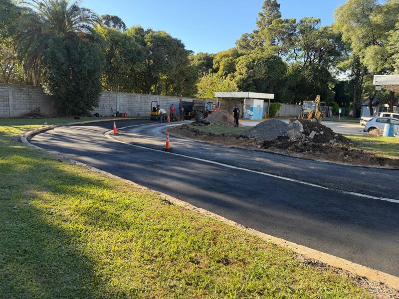 Pavimentación asfáltica en curva con conos de señalización y retroexcavadora al fondo