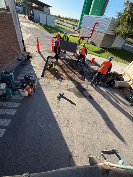 Cuadrilla de operarios con chalecos y cascos trabajando con compactador en planta industrial