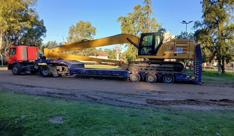 Excavadora CAT con logo Caminos Paitz sobre trailer de transporte con camión rojo